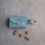 Light blue leather dog treat pouch with a snap flap stamped LUNA and small dog treats on grey plaster