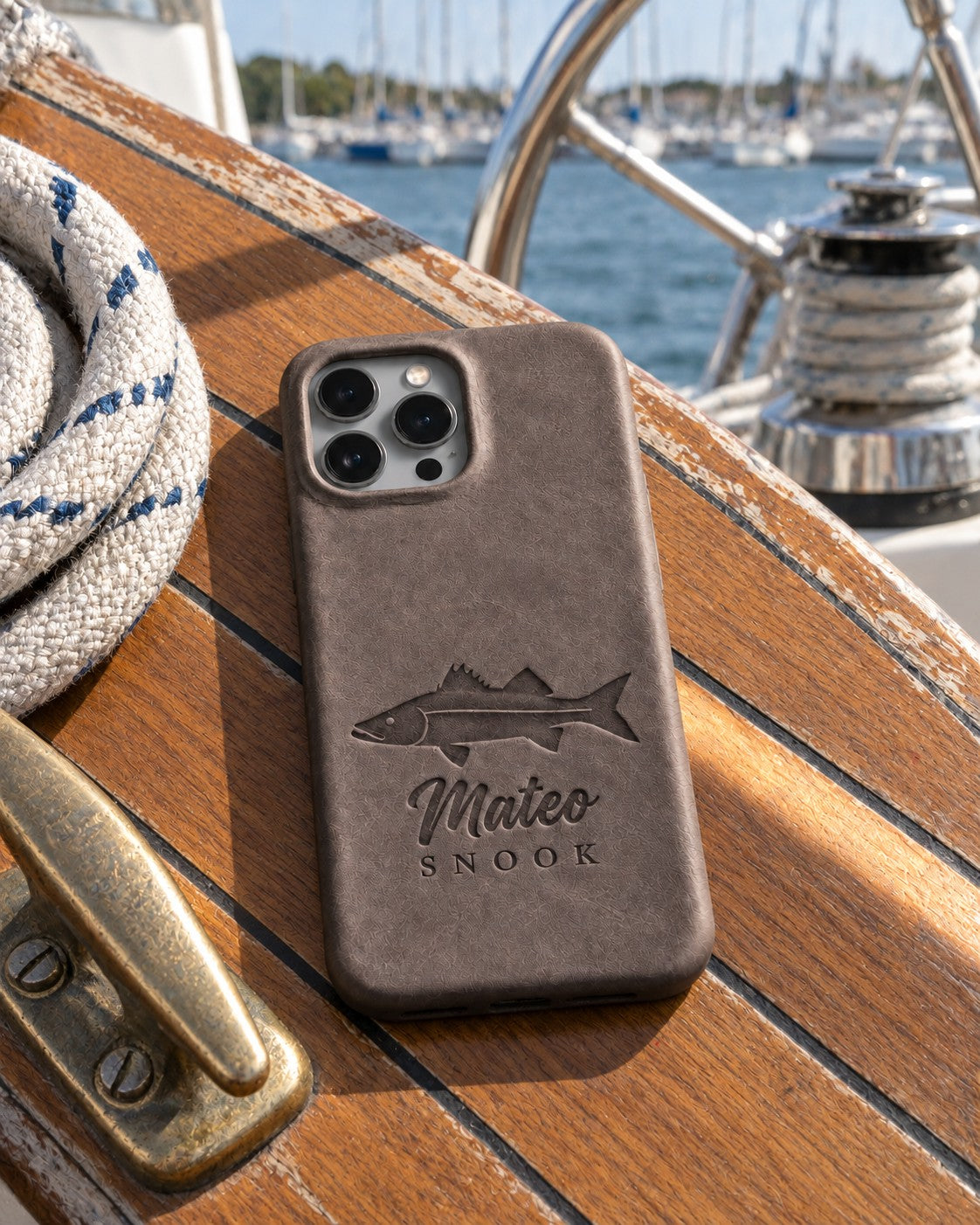 Country Gray Mateo SNOOK iPhone case in full-grain leather on the worn teak cockpit table of a sailboat beside a coiled white dock line