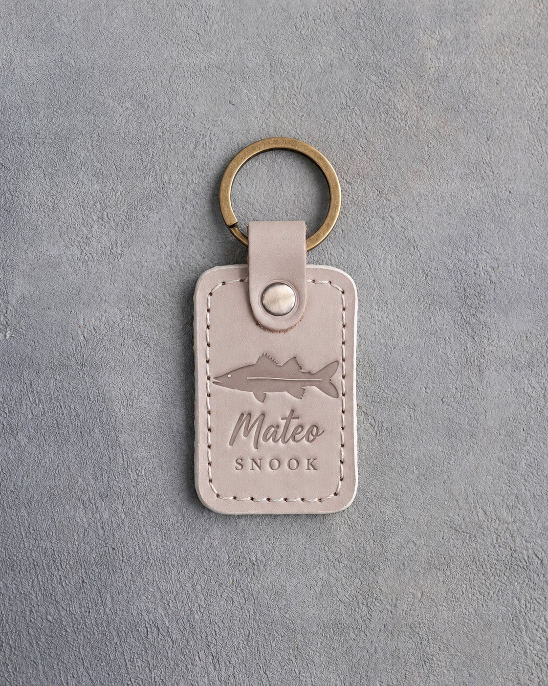 Gray Sand leather keychain debossed with a snook above Mateo and SNOOK, on gray plaster