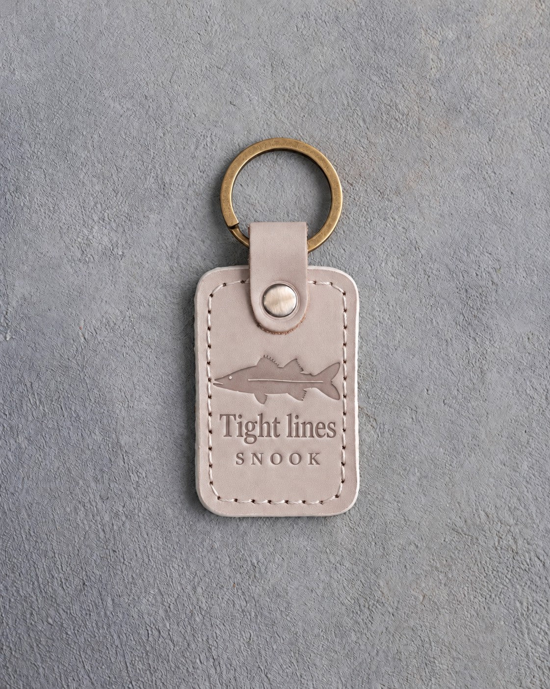 Gray Sand leather keychain debossed with a snook above Tight lines and SNOOK, on gray concrete