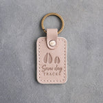 Gray sand leather keychain debossed with a large deer track and a small fawn track above the words Snow day TRACKS, on gray plaster