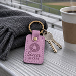 Lilac Soccer Mom keychain on car keys beside a pair of small cleats on a sideline blanket