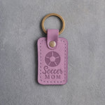 Lilac leather keychain debossed with a soccer ball and the words Soccer MOM, on gray plaster