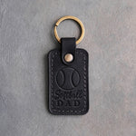 Black leather keychain debossed with a softball and the words Softball DAD, on gray plaster