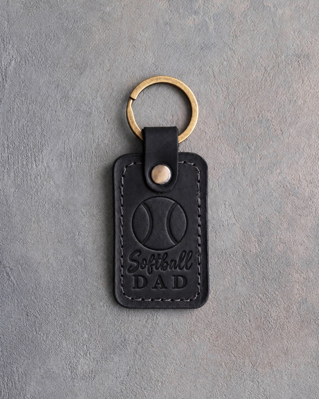 Black leather keychain debossed with a softball and the words Softball DAD, on gray plaster