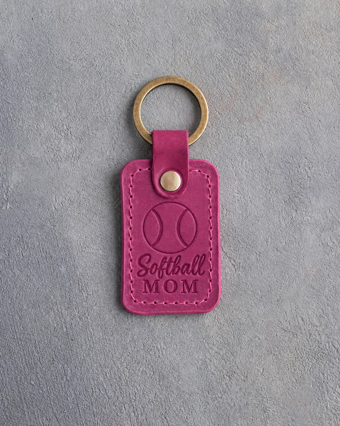 Fuchsia pink leather keychain debossed with a softball and the words Softball MOM, on gray plaster
