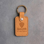 Golden tan leather keychain debossed with a guitar pick above the words Spare picks IN THE COUCH, on gray plaster