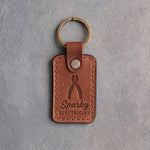 Copper-toned leather keychain debossed with upright lineman's pliers above the words Sparky and ELECTRICIAN, on gray plaster