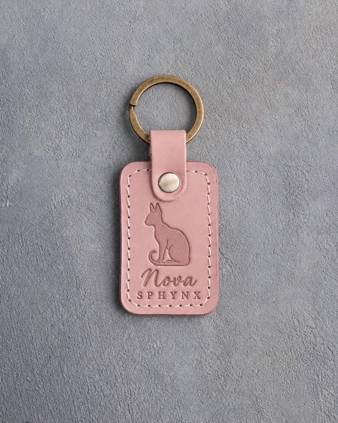 Blush pink leather keychain debossed with a sitting Sphynx cat with large ears above the name Nova and SPHYNX