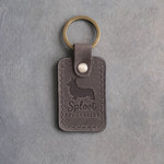 Country gray leather keychain with a debossed corgi silhouette and the words Sploot SPECIALIST on gray concrete