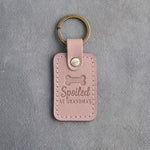 Blush pink leather keychain debossed with a dog biscuit and the words Spoiled AT GRANDMA'S, on gray concrete