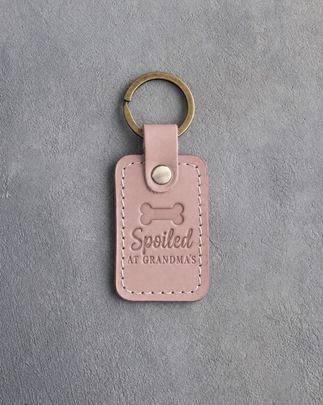 Blush pink leather keychain debossed with a dog biscuit and the words Spoiled AT GRANDMA'S, on gray concrete