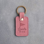 Pink Parisian Blossom leather keychain debossed with a pennant and the words Sports MOM, on gray plaster