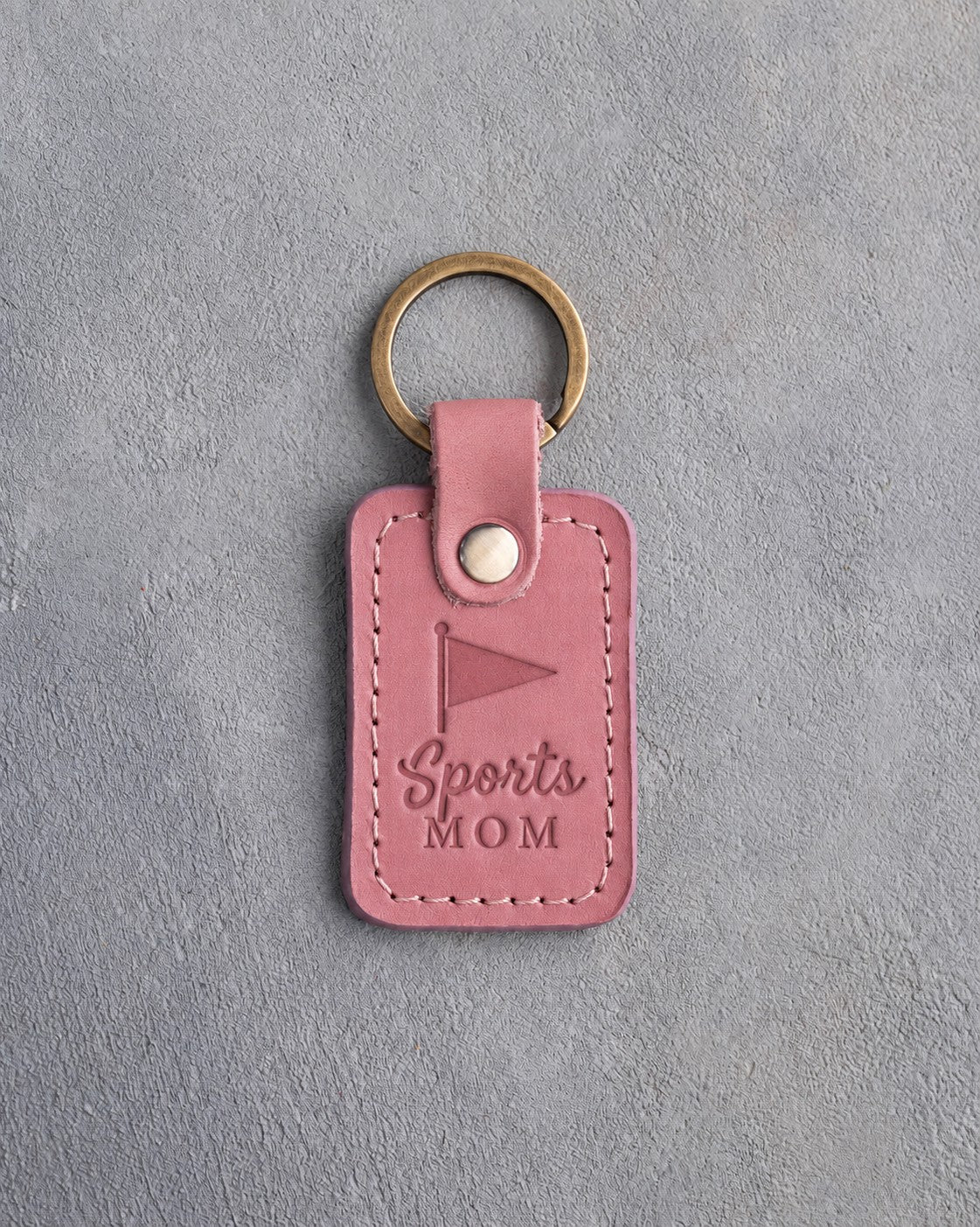 Pink Parisian Blossom leather keychain debossed with a pennant and the words Sports MOM, on gray plaster