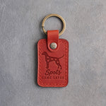 Poppy red leather keychain debossed with a Dalmatian silhouette and the words Spots CAME LATER, on gray concrete