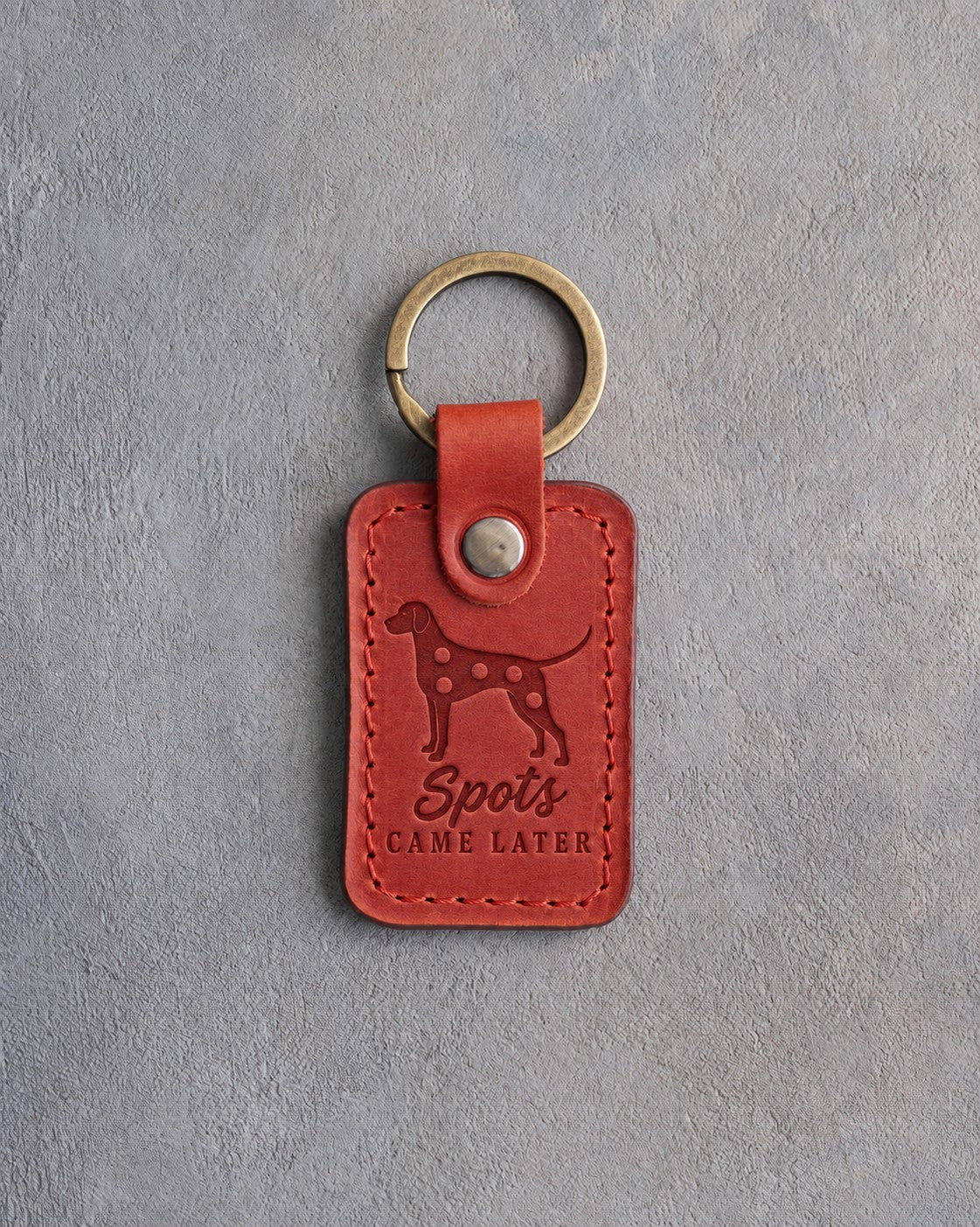 Poppy red leather keychain debossed with a Dalmatian silhouette and the words Spots CAME LATER, on gray concrete