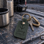 Green Spring Gobbler keychain resting on a turkey vest beside a slate call in fresh spring grass