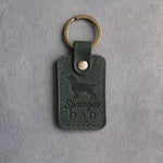 Forest green leather keychain debossed with a springer spaniel silhouette and Springer DAD on gray concrete