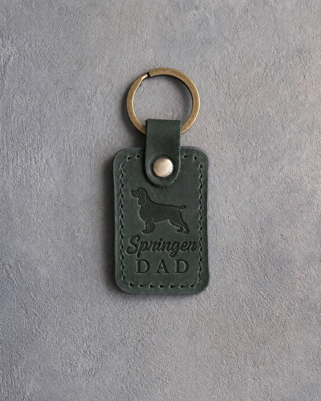 Forest green leather keychain debossed with a springer spaniel silhouette and Springer DAD on gray concrete