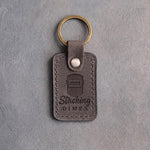 Country gray leather keychain debossed with a welding hood above the words Stacking and DIMES, on gray plaster