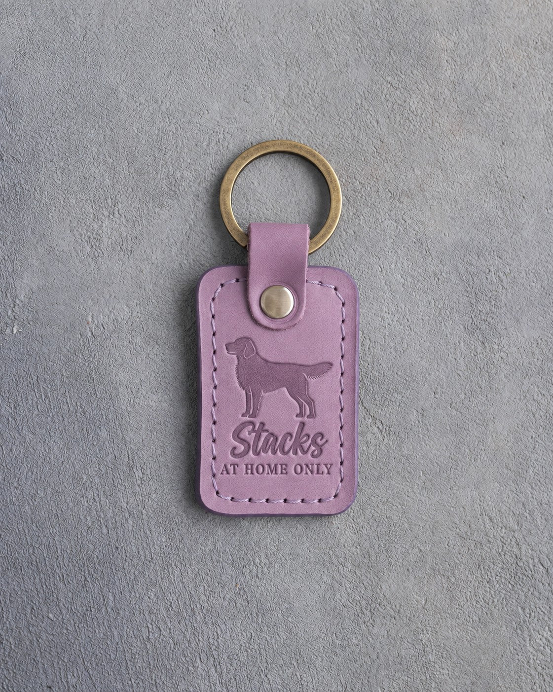 Lilac leather keychain debossed with a dog in a show stack and the words Stacks AT HOME ONLY, on gray concrete