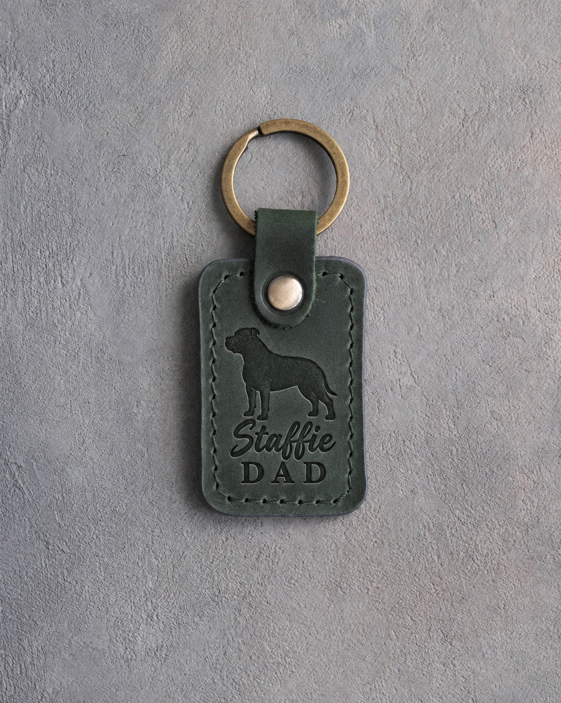 Forest green leather keychain debossed with an American Staffordshire Terrier silhouette and the words Staffie DAD, on gray concrete