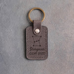 Country gray leather keychain debossed with the Orion constellation above Stargazer and CLEAR SKIES, on gray concrete
