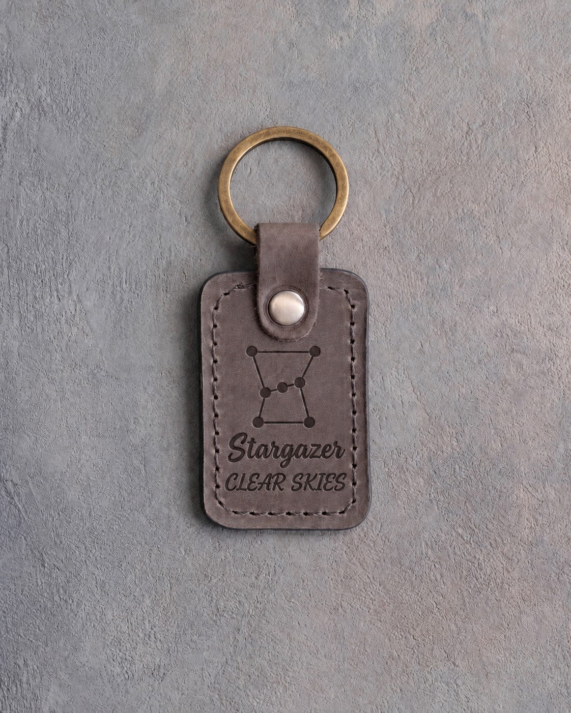 Country gray leather keychain debossed with the Orion constellation above Stargazer and CLEAR SKIES, on gray concrete