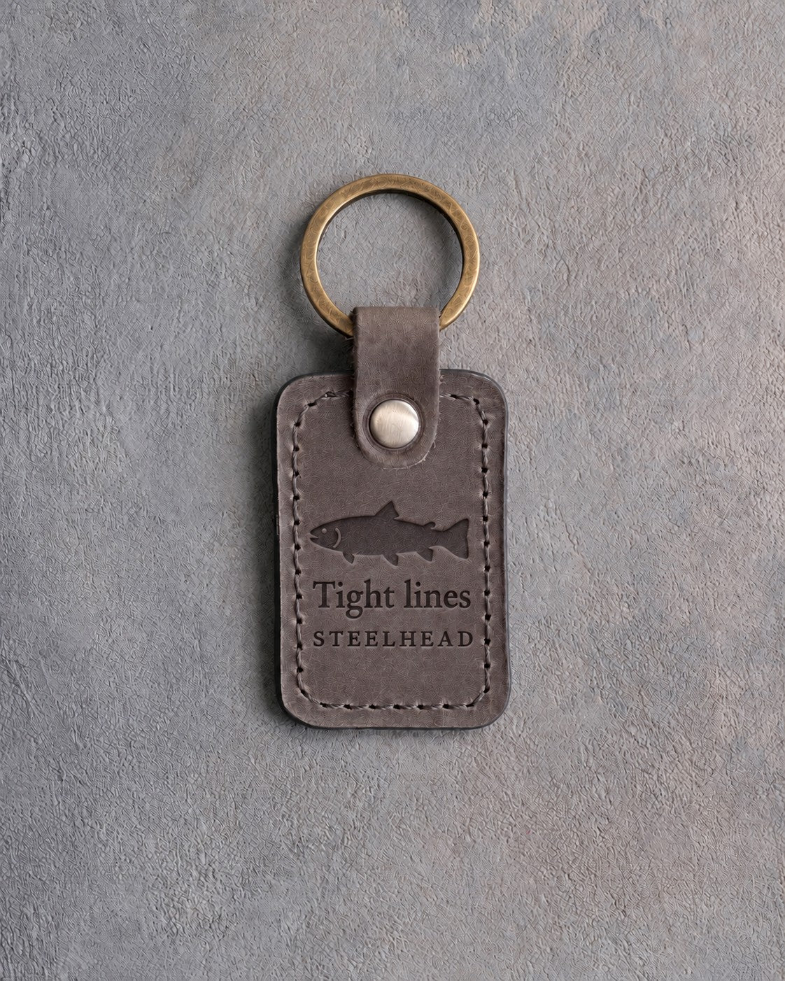Country Gray leather keychain debossed with a steelhead above Tight lines and STEELHEAD, on gray concrete
