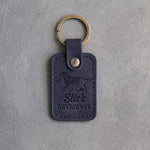 Blueberry navy leather keychain debossed with a golden retriever carrying a stick and the words Stick RETRIEVER, on gray concrete