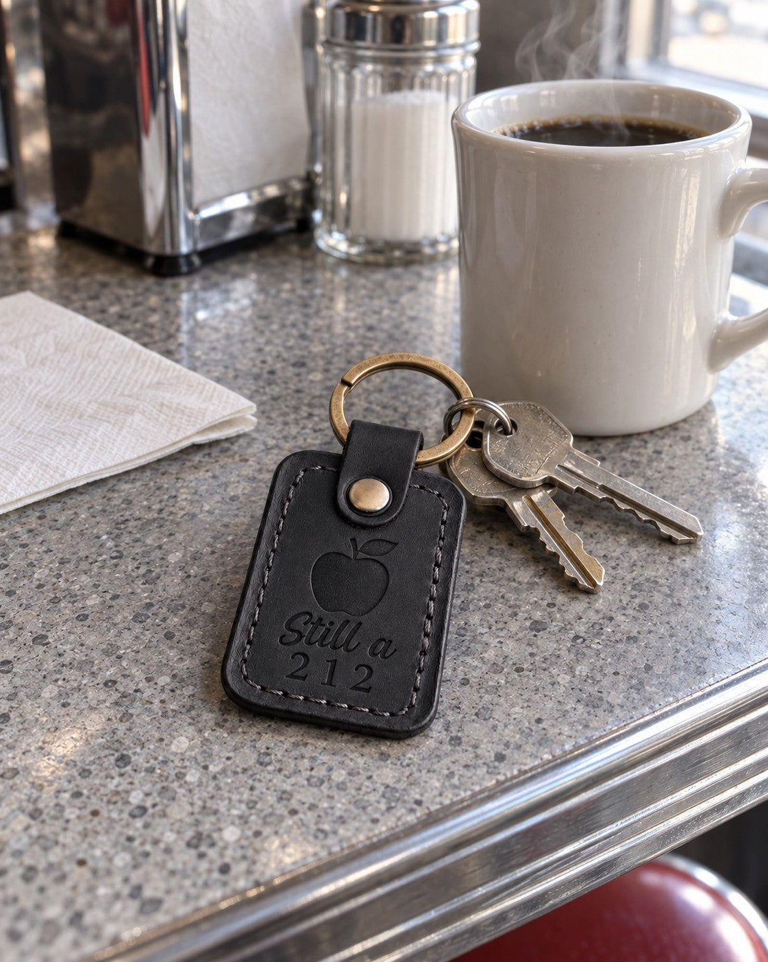 Black Still a 212 keychain on apartment keys resting on a subway map in a city cafe
