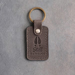 Country gray leather keychain debossed with a whitetail deer track above the words Still HUNTING, on gray plaster