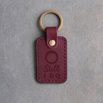Sangria red leather keychain debossed with a single wedding band above the words Still I DO, on gray concrete