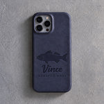 Back of a blueberry leather iPhone case debossed with a striped bass above Vince and STRIPED BASS below the camera, on gray plaster