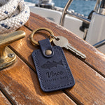 Blueberry Vince STRIPED BASS keychain in full-grain leather on the worn teak cockpit table of a sailboat beside a coiled white dock line