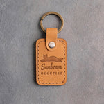 Indian summer amber leather keychain debossed with a cat sprawled flat above the words Sunbeam OCCUPIED