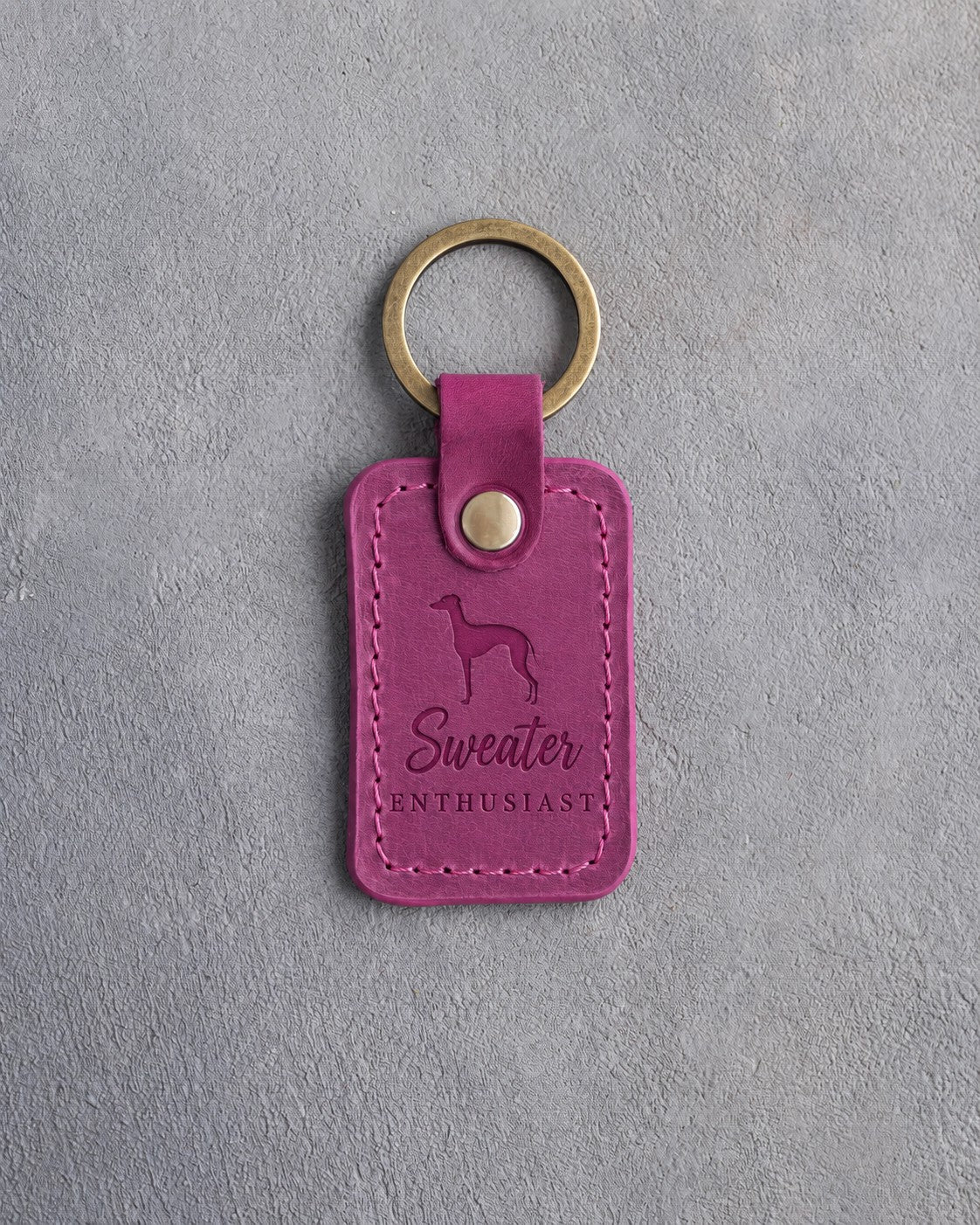 Fuchsia pink leather keychain debossed with an Italian Greyhound silhouette and the words Sweater ENTHUSIAST, on gray concrete