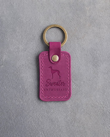 Fuchsia pink leather keychain debossed with an Italian Greyhound silhouette and the words Sweater ENTHUSIAST, on gray concrete