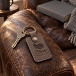 Oliver TABBY CAT keychain in gray leather on a sunny window seat beside a folded blanket