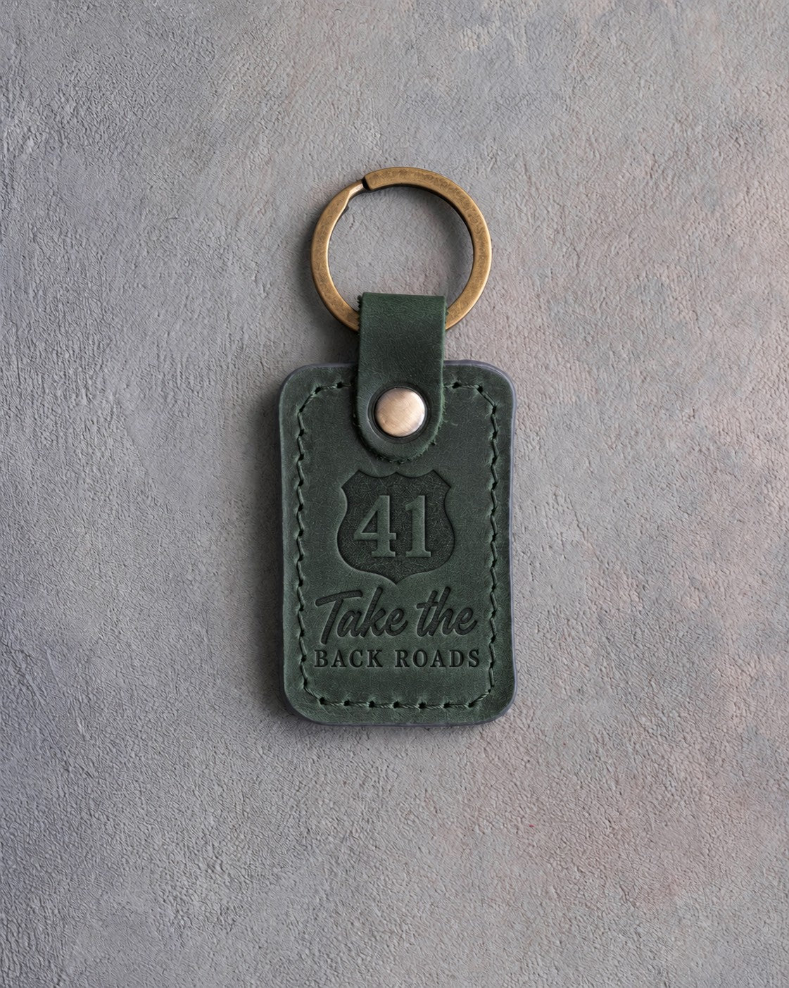 Forest green leather keychain debossed with a route shield numbered 41 above Take the and BACK ROADS