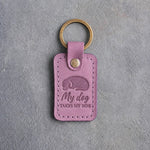 Lilac leather keychain debossed with a curled sleeping dog above My dog and TAKES MY SIDE, on gray concrete