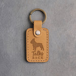 Indian Summer tan leather keychain debossed with a French bulldog silhouette and the words Talks BACK, on gray concrete