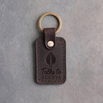 Dark espresso leather keychain debossed with a single leaf above Talks to PLANTS, on gray concrete