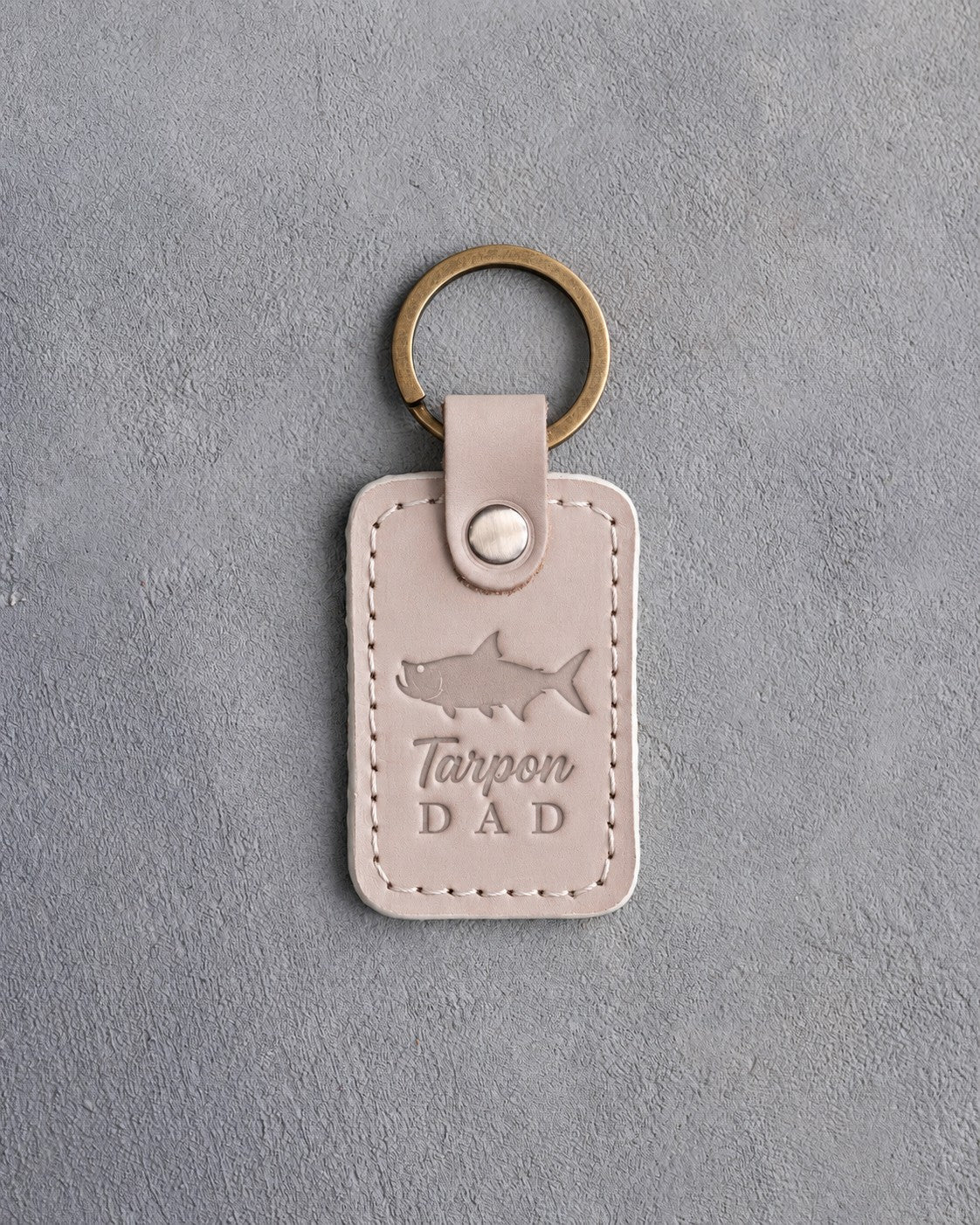 Gray sand leather keychain debossed with a tarpon above the words Tarpon DAD, on gray plaster
