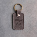 Country gray leather keychain debossed with a tarpon above Reid and TARPON, on gray plaster
