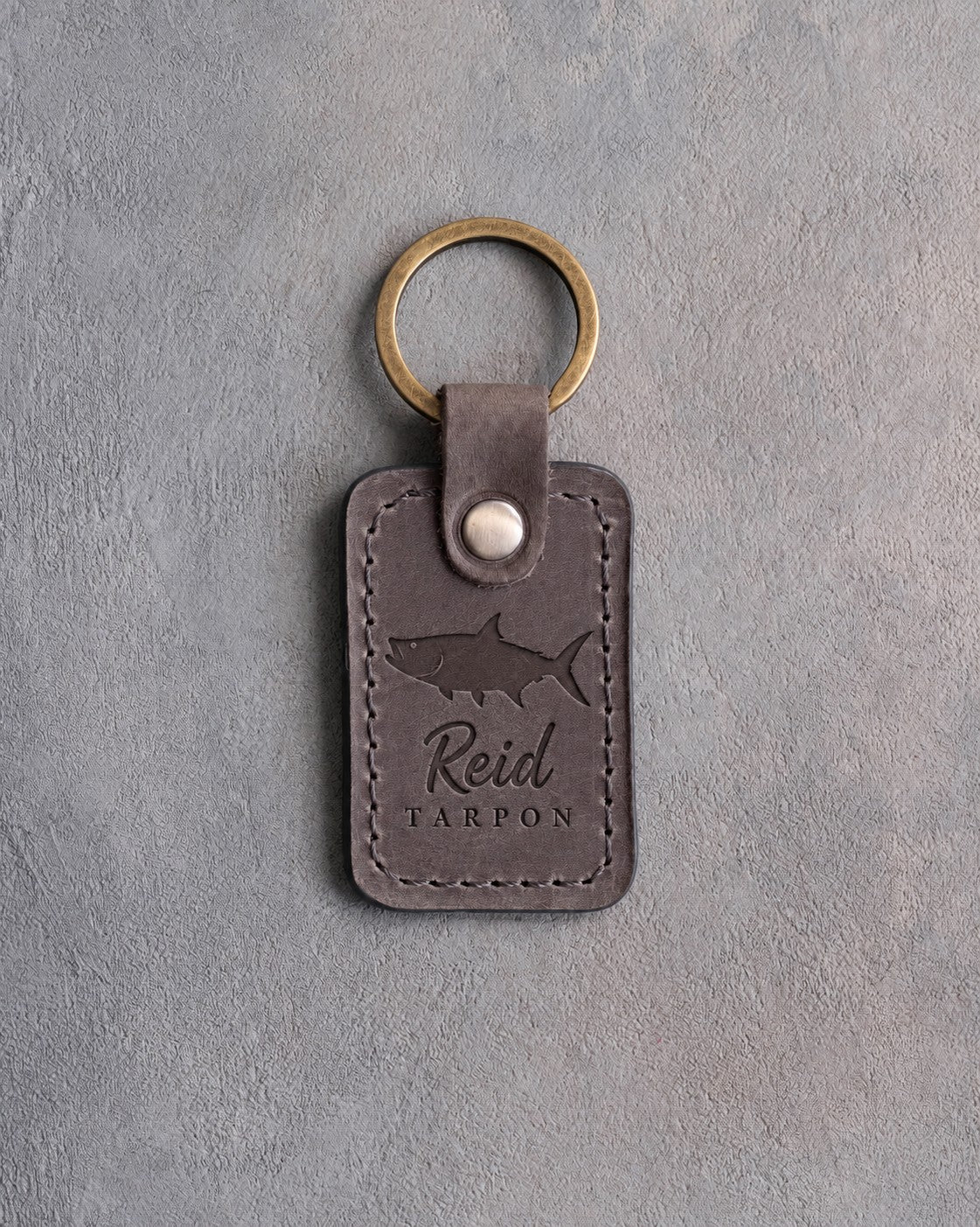 Country gray leather keychain debossed with a tarpon above Reid and TARPON, on gray plaster
