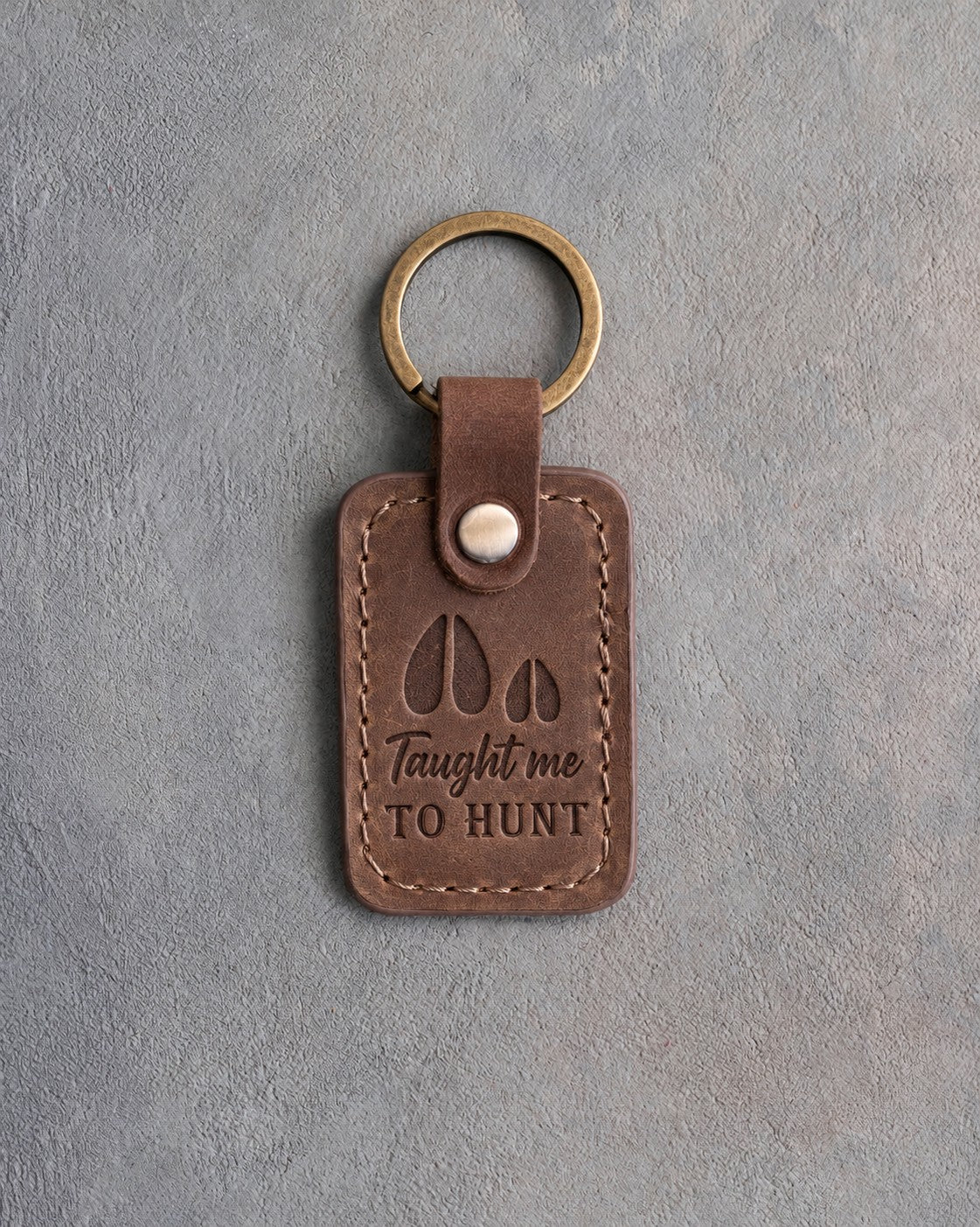 Sicilian brown leather keychain debossed with a deer track and a fawn track above the words Taught me TO HUNT, on gray plaster