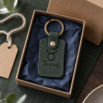 Green Taurus keychain on a key ring resting beside a potted plant on a sunlit windowsill