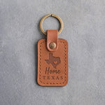 Caramel leather keychain debossed with a solid Texas silhouette and a small heart at Austin above Home and TEXAS, on gray concrete