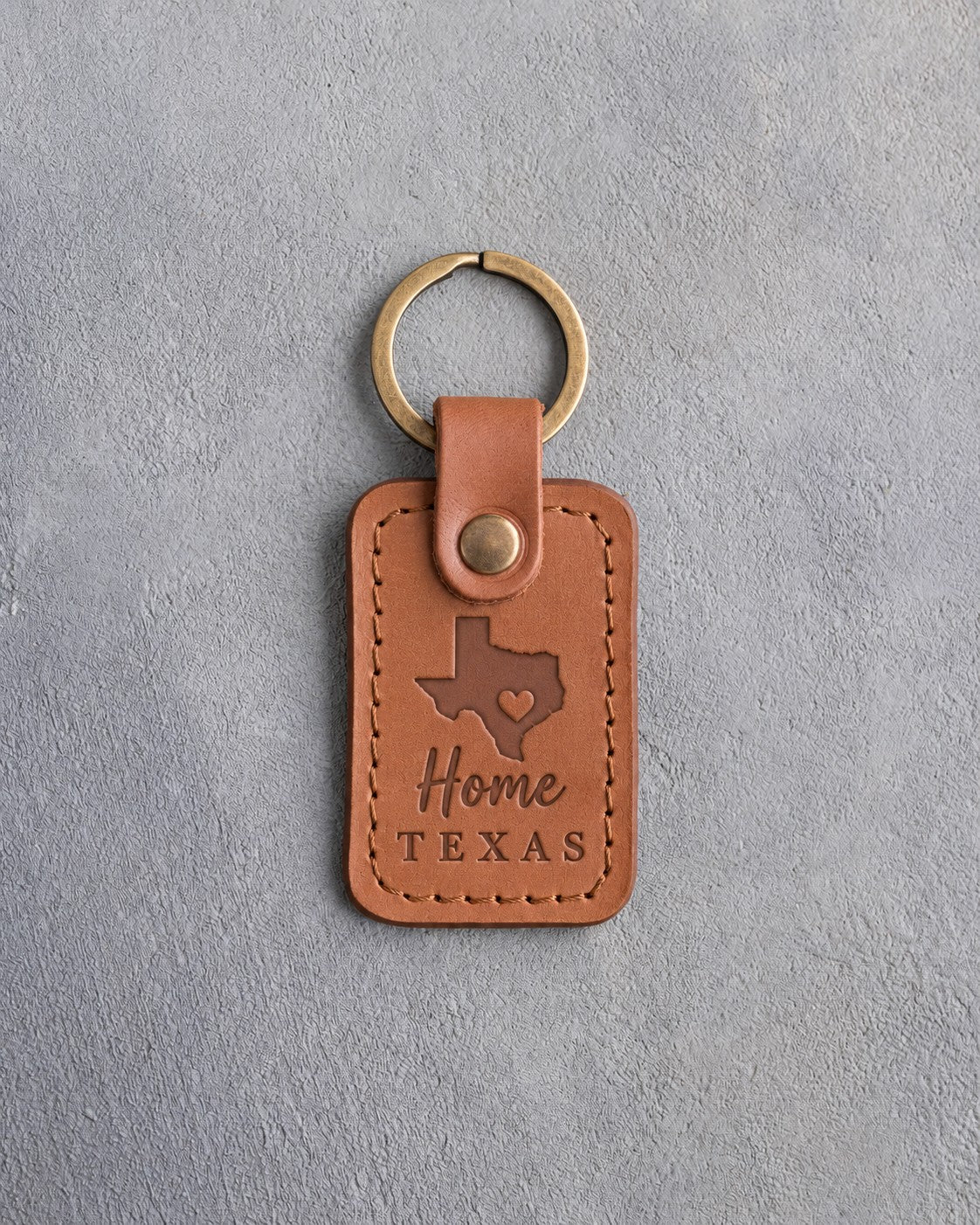 Caramel leather keychain debossed with a solid Texas silhouette and a small heart at Austin above Home and TEXAS, on gray concrete